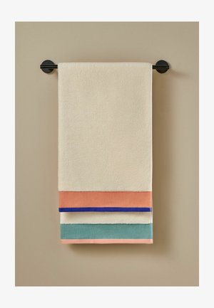 Toalla beige con bloques de color coral, azul y verde colgada en una barra negra de toallas montada en la pared contra una pared beige.