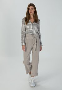 Lightweight, long-sleeve blouse with a geometric black and white pattern; paired with high-waisted, beige wide-leg trousers and white sneakers.