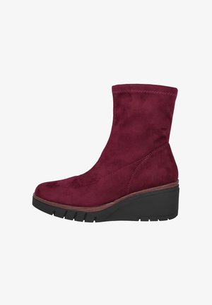 Botín de ante burdeos con una textura suave, puntera redondeada y suela en cuña con una base de goma negra y detalles de costura sutiles.