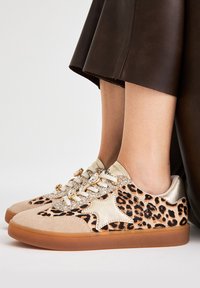Zapatillas de leopardo con detalles en ante beige y brillos dorados. Suelas de goma y cordones adornados con acentos metálicos.