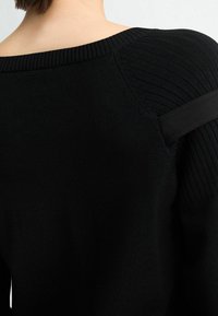 Pull noir en maille avec une texture côtelée sur les épaules et un large décolleté. Tissu lisse, design minimaliste, avec une silhouette ajustée.