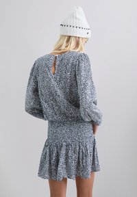 Vestido de estampado floral en navy y blanco, con mangas largas, cintura fruncida y dobladillo con volantes; presenta un detalle en forma de llave en la parte posterior.