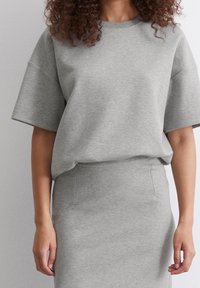 Szara bawełniana bluza z szerokimi, krótkimi rękawami, zestawiona z dopasowaną szarą spódnicą. Miękka faktura, luźny styl, bezszwowa konstrukcja.