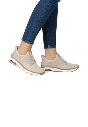 Baskets de sport beiges avec tige en mesh, design à lacets, accents beiges subtils et amorti visible dans la semelle. Portées avec un jean noir.
