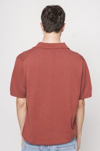 Polo cu mânecă scurtă de culoare ruginită, cu guler ribbed și accente pe umeri, realizat dintr-un material tricotat moale, cu o textură netedă.