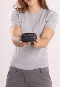 Schwarzes, krokodilgeprägtes Leder-Make-up-Täschchen mit goldenem Reißverschluss, gehalten in Händen. Die Abmessungen sind kompakt; verfügt über eine embossed Markenprägung auf der Vorderseite.