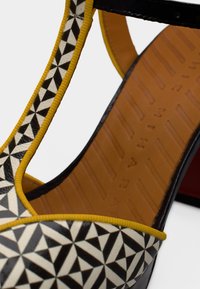 Ανδρικό τακούνι σε ασπρόμαυρο με γεωμετρικό σχέδιο. Διαθέτει κίτρινο περίγραμμα και λείο ταμπά πέλμα με υφή στη βάση για καλύτερη πρόσφυση.