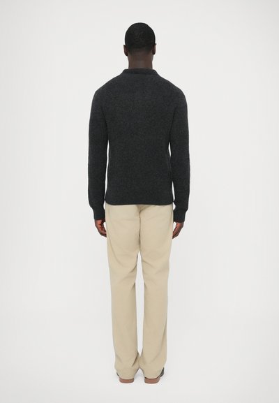 Sötétszürke kötött pulóver laza szabással, kerek nyakkivágással és bordázott mandzsettákkal, világos bézs egyenes szárú nadrággal párosítva.