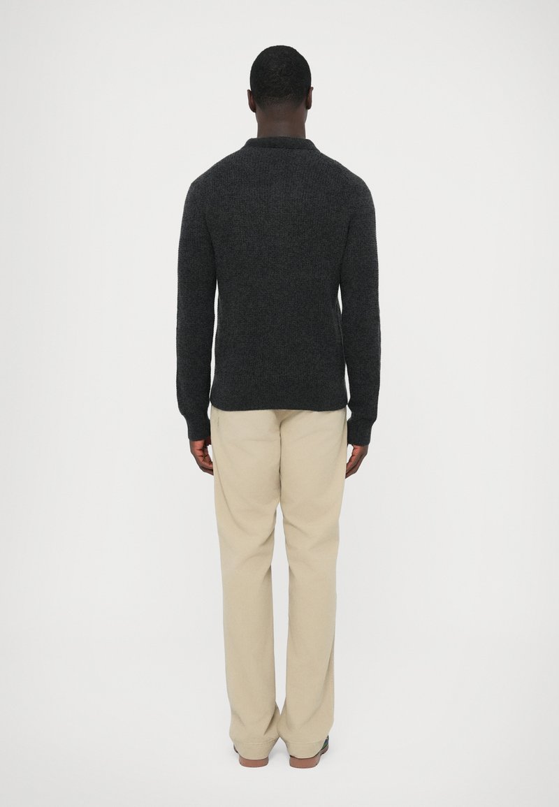 Maglione grigio scuro lavorato a maglia con vestibilità comoda, collo rotondo e polsini a coste, abbinato a pantaloni beige chiaro a gamba dritta.