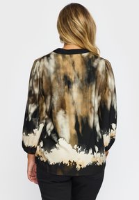 Løst siddende bluse med et tie-dye mønster i brune, cremede og sorte farver, med en sort halsudskæring og puffede ærmer.