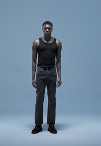 Svart tanktop, mørke jeans og svarte støvler. Figuren står mot en lys blå bakgrunn og viser frem et enkelt, tettsittende design.