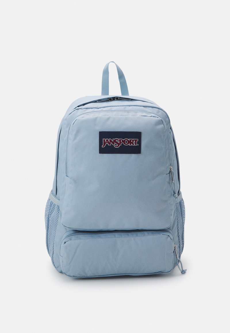 Mochila Jansport de color azul claro con dos compartimentos con cremallera, bolsillos laterales de malla y un asa de transporte en la parte superior. Textura de tela suave.