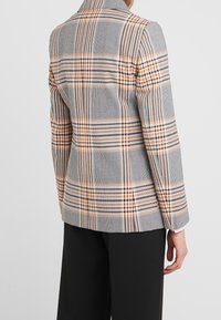 Grijze gestreepte blazer met oranje en blauwe lijnen, getailleerde pasvorm, pieklapels en een zachte textuur. Zwarte broek zichtbaar onderaan.