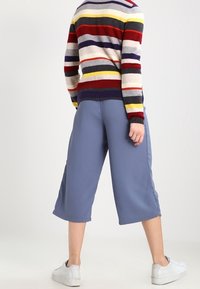 Helleblaue Culotte-Hosen mit lockerer Passform, glatter Textur und seitlichen Schlitzen, kombiniert mit einem mehrfarbigen gestreiften Pullover und weißen Sneakern.