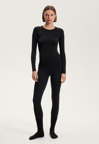 Zwart langemouwen top en legging set, gladde textuur, aansluitend ontwerp, met geribbelde zwarte sokken, wat een monochromatische uitstraling creëert.