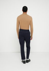 Μπλούζα από πλεκτό ύφασμα με μακριά μανίκια σε ταμπά απόχρωση, συνδυασμένη με σκούρο μπλε, καλοραμμένο παντελόνι. Ορατά μαύρα παπούτσια και λευκές κάλτσες. Λείο ύφασμα και εφαρμοστή σχεδίαση.