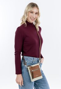 Krosová taška s tělem ze světle béžového nylonu, hnědými koženými akcenty a přední kapsou na zip. Obsahuje hnědý popruh a stříbrné kovové prvky.