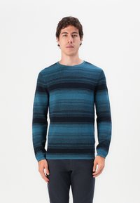 Blå og svart stripete langermet genser med rund hals og teksturert stoff, båret av en modell mot en enkel hvit bakgrunn.