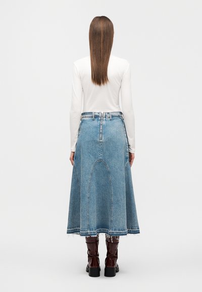 Τζιν φούστα με φαρδιά γραμμή, ανοιχτό μπλε χρώμα, ξέφτια τελείωμα και καμπυλωτές ραφές. Συνδυάζεται με καφέ μπότες μέχρι το γόνατο.