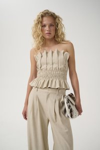 Haut sans bretelles beige à côtes avec une taille smockée et un ourlet évasé, associé à un pantalon plissé taille haute et une pochette en fourrure à motifs.