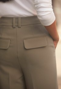 Bežid kohandatud püksid tagakottidega, sile tekstuur ja vööpaelad. Kombineeritud slim fit valge pika varrukaga särgiga.