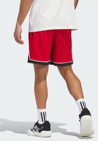 Röda idrottsshorts med svarta detaljer och vit piping, kombinerat med svarta sportskor och vita strumpor med svarta ränder.