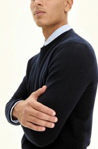 Granatowy sweter z miękkiego materiału, z okrągłym dekoltem i ściągaczami, noszony na jasnoniebieskiej koszuli z kołnierzykiem.