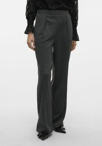 Pantaloni grigi su misura con gamba larga, caratterizzati da un tessuto testurizzato, pieghe frontali e vita alta. Abbinati a scarpe nere a punta.