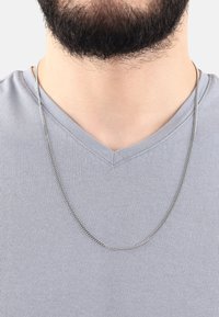 Silver kedja hängande på en ljusgrå t-shirt med v-ringning. Kedjan har en slät, glänsande yta och en medelhård tjocklek.