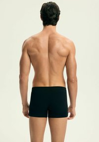 Czarne bokserki z miękkiego materiału, o minimalistycznym designie, elastycznej talii i dopasowanej sylwetce, prezentowane na plecach męskiego modela.