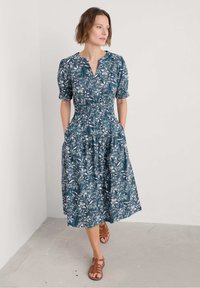 Tyrkysové květinové midi šaty s nabíranými rukávy, smocked pasem, bočními kapsami a knoflíkovým výstřihem, doplněné hnědými páskovými sandály.