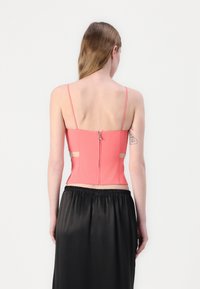 Coral backless top with thin straps, zip closure, and cutout details, paired with a flowing black satin skirt. Smooth texture and fitted design.