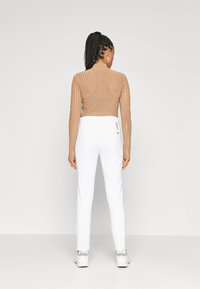 Brūns ribots garais piedurknes tops, savienots ar baltām biksēm. Bikses ir šauras un ar gludu tekstūru, ar vieglu spīdumu.