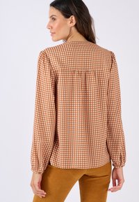 Blusa lunga a maniche lunghe a quadretti marrone con scollatura rotonda, dettagli arricciati sul retro e polsini aderenti, realizzata in tessuto leggero.