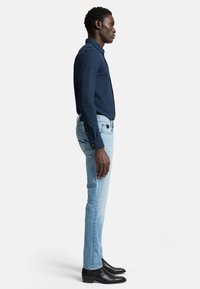 Camicia a maniche lunghe blu navy con colletto, abbinata a jeans blu chiaro e stivali in pelle nera, mostrata in vista laterale.