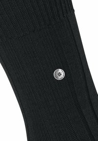 Czarne skarpetki z prążkowanego dzianiny z małym metalicznym logo. Materiał wydaje się miękki, o gładkiej teksturze i jednolitym wzorze.