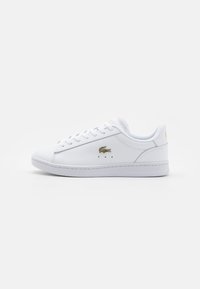 Sneaker din piele albă cu design cu șireturi, av�ând un mic logo auriu pe lateral și perforații subtile pentru ventilație.