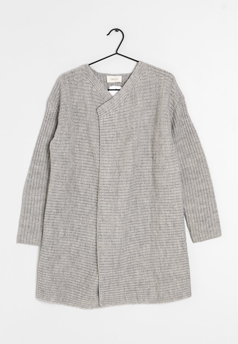 Cardigan long en tricot gris clair avec des manches côtelées et un devant asymétrique, accroché à un cintre noir sur fond blanc.