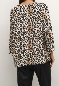 Top con stampa leopardata caratterizzato da un fit morbido, maniche a tre quarti e scollatura tonda, realizzato in tessuto morbido e leggero nelle tonalità beige, nero e marrone.