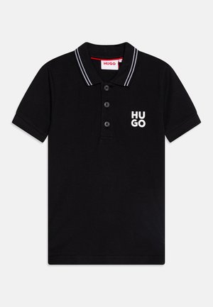 Polo noir à manches courtes avec le logo "HUGO" blanc sur la poitrine, trois boutons noirs et un col noir avec des bandes blanches.