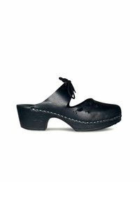 Zwarte leren klomp met een gebogen hak, uitsnijdingen in bloemdesign en witte stiksels langs de zool. Bevat een strik aan de voorkant.