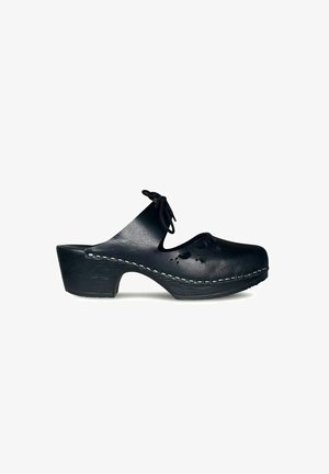 Zwarte leren klomp met een gebogen hak, uitsnijdingen in bloemdesign en witte stiksels langs de zool. Bevat een strik aan de voorkant.