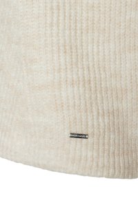 Strickmütze aus weicher cremefarbener Wolle, mit geripptem Muster und einem kleinen schwarzen Etikett mit "MADE IN MORE" an der Seite als Detail.