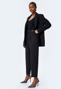 Czarna marynarka noszona na czarnym podkoszulku, zestawiona z dopasowanymi czarnymi spodniami z błyszczącym złotym akcentem. Całość uzupełniają szpilki w leopardzim wzorze.