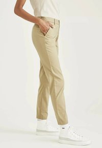 Chino beige con vestibilità slim, tasche laterali e cuciture a vista, abbinati a sneakers alte bianche. Tessuto di cotone morbido, design pulito.