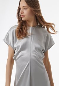 Zilver satijnen jurk met een relaxte pasvorm, korte mouwen, een ronde hals en subtiele draping aan de zijkanten. Glad textuur en minimaal ontwerp.