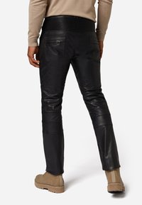 Zwarte leren broek met geribde elastische tailleband, voorzien van twee achterzakken en contrasterende paneeldetails op de benen.