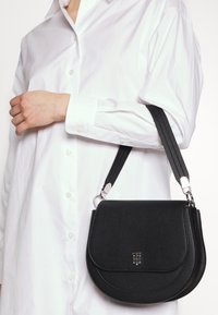 Borsa a tracolla nera in pelle con finitura texturizzata, patta arrotondata e hardware in argento. Tracolla regolabile per un utilizzo versatile.