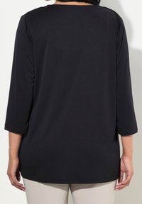 Musta kolmeneeljandiku varrukatega topp ümmarguse kaelusega ja laia lõikega, valmistatud siledast, venivast kangast. Ilma nähtavate mustrite või aksessuaarideta.