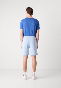 T-shirt bleu à col rond et shorts bleu clair. Les shorts sont dotés d'une taille élastique et d'une poche au dos. Les chaussures sont blanches avec des accents gris clair.